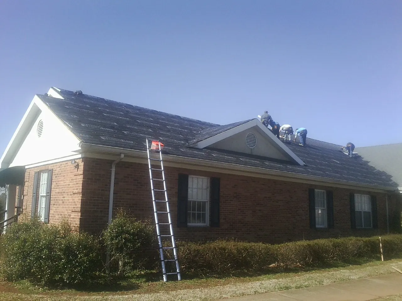 Crew tearing shingles off a brick ranch roof with a ladder set — Emergency Roof Repair work by our crew in Branchville
