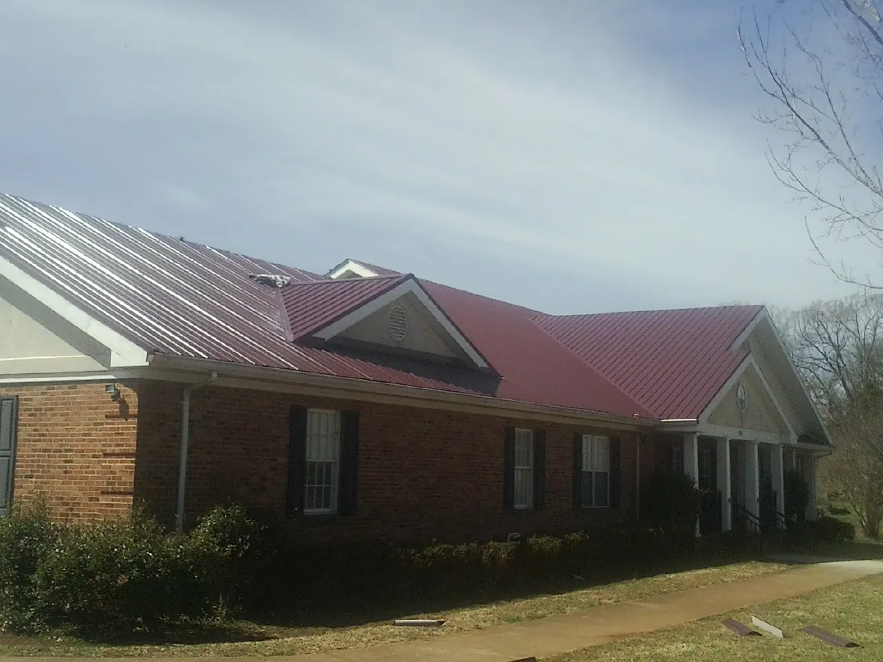Red metal roof with gabled entries on a long brick building, from a Hail Damage Roof Repair job in Branchville