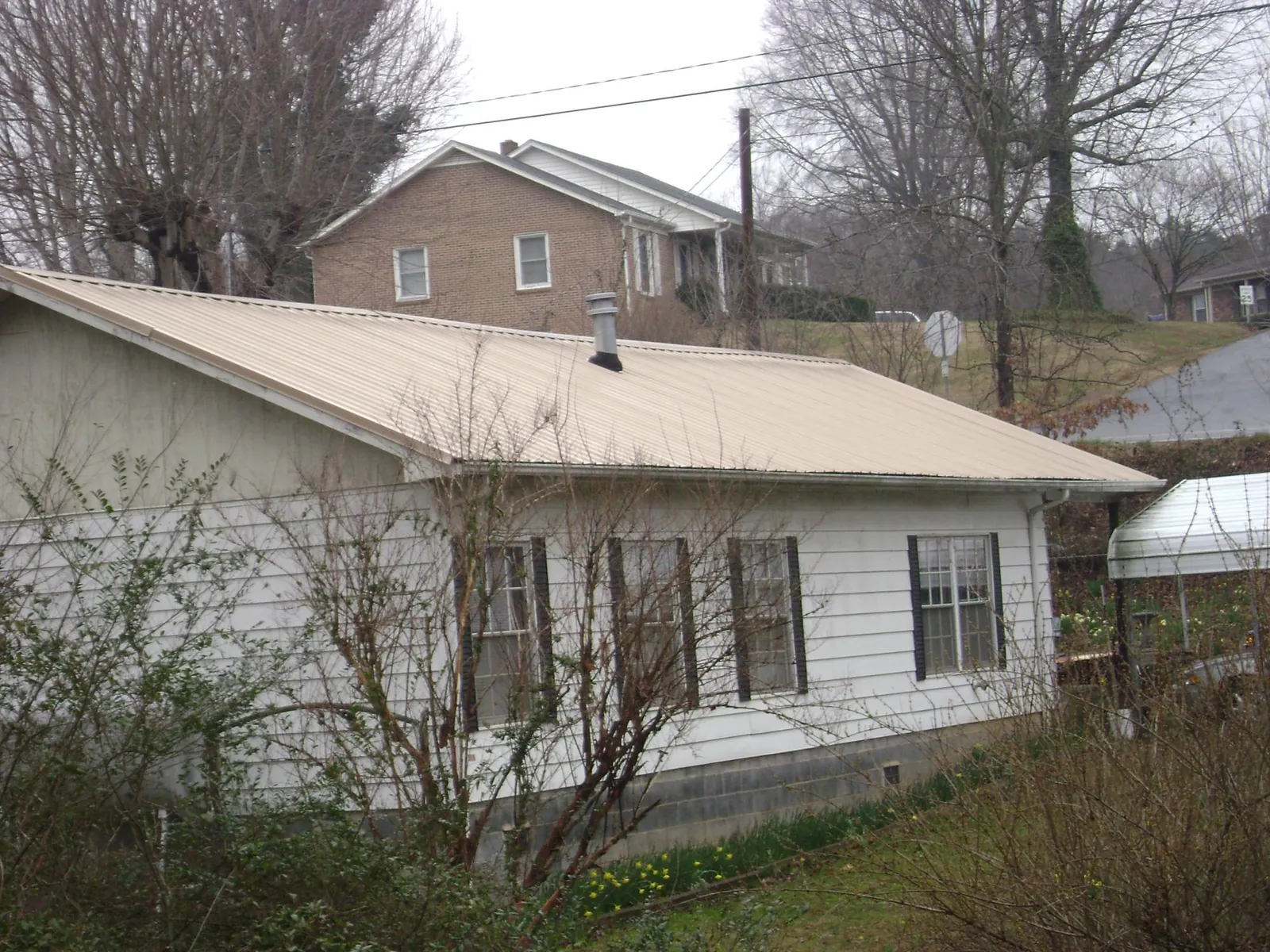 Tan metal roof on a white sided house set into a hillside — Commercial Roofing by Roofing Brothers in Branchville
